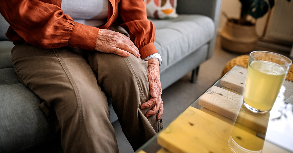Close up of elderly persons hands clutching leg in pain while sitting on couch