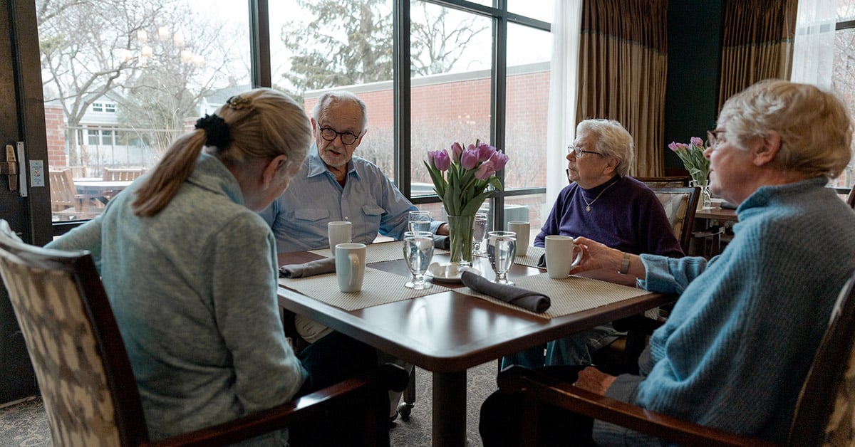 Group of seniors sit around dining table in senior living community
