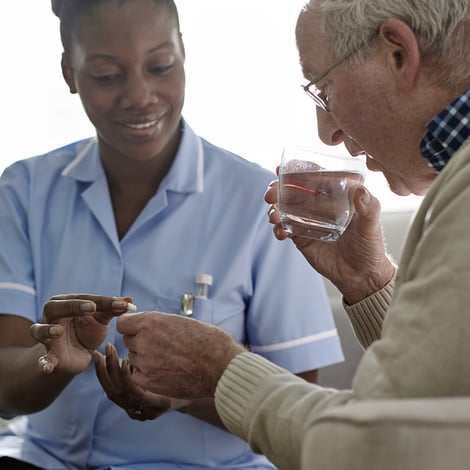 Nurse hands medicine to a senior man with a water glass 