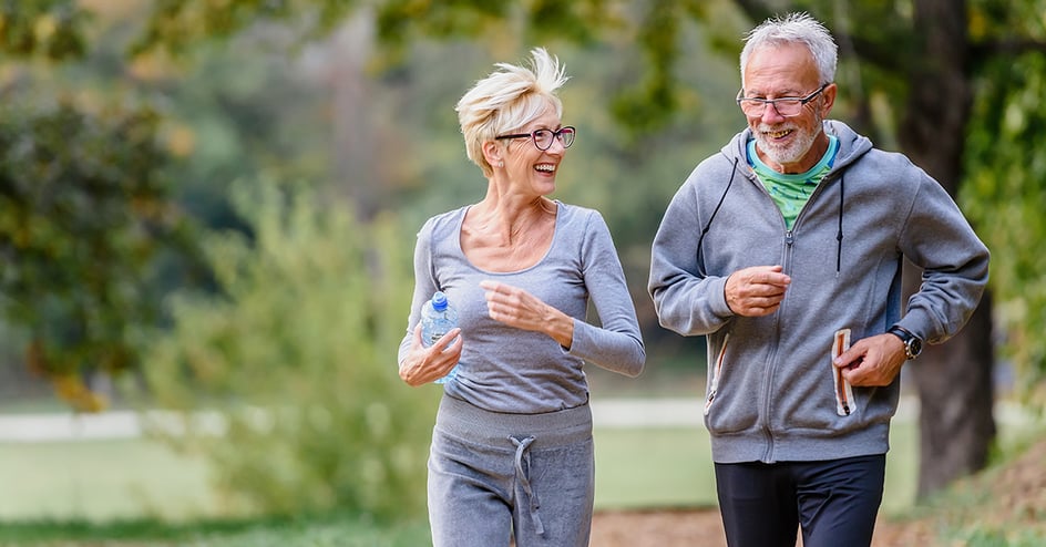 Senior man and woman jog and smile on trail