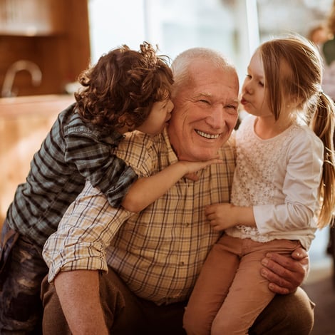 Senior man holds granddaughter while grandson kisses his cheek
