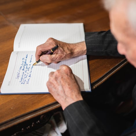 Senior man writes in journal with a pen at office table