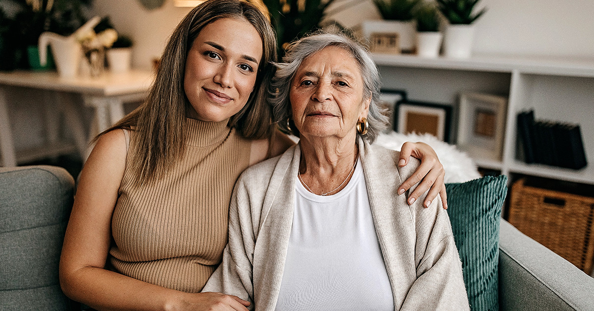 Senior woman and daughter sit on couch looking at camera