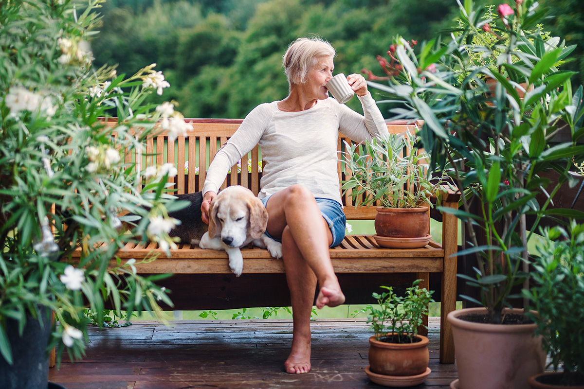 Senior woman sitting on a bench drinking coffee with dog