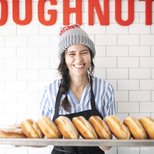 Woman in hat and apron holds tray of donuts