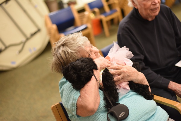 resident hugging small black dog in a dress