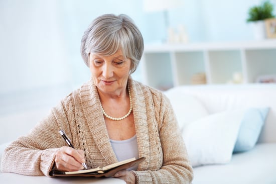 older woman sitting on couch writing in journal