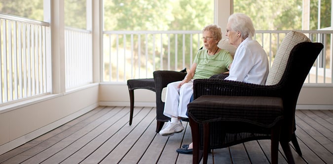 Two elderly women sit on chairs on a porch in summer