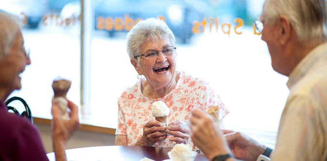 Three seniors laugh while eating ice cream cones at restaurant
