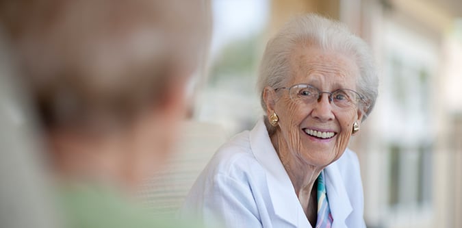 Elderly woman in white smiles at man sitting across from her