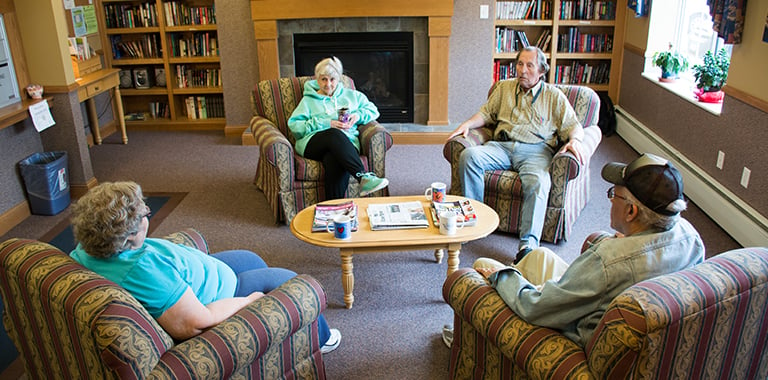 Elderly group sits in chairs around coffee table 