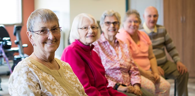 Five elderly residents smiling while sitting in community room