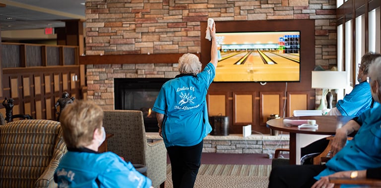 Senior in bowling shirts plays electronic bowling on lounge television