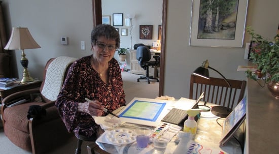 resident painting a watercolor painting and smiling at camera