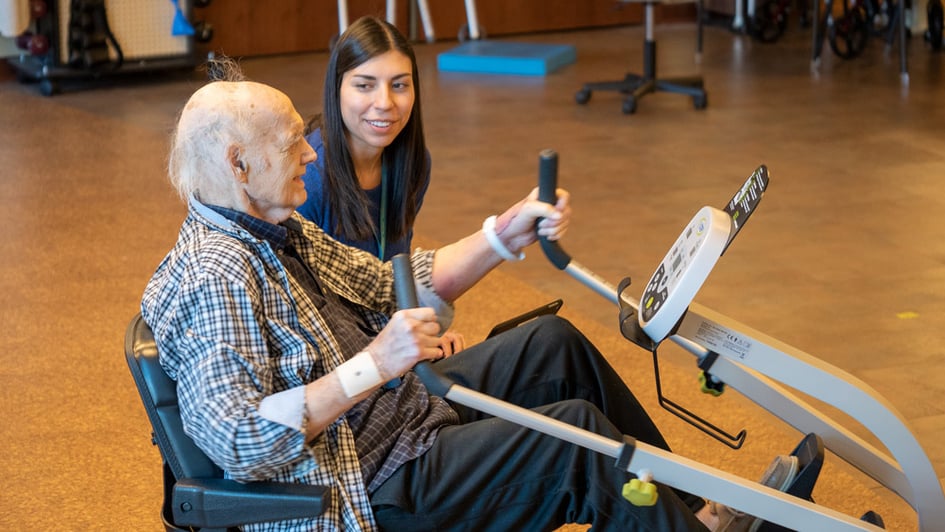 senior on an exercise machine with a physical therapist helping them