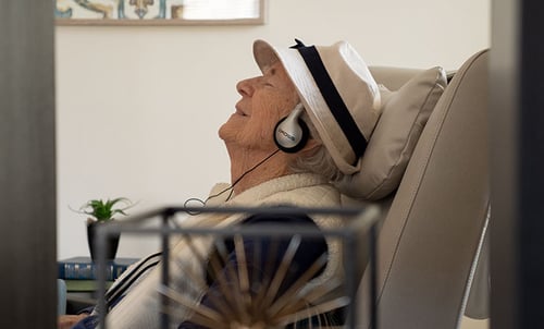 elderly man sitting in char, listening to music with headphones and his eyes are closed