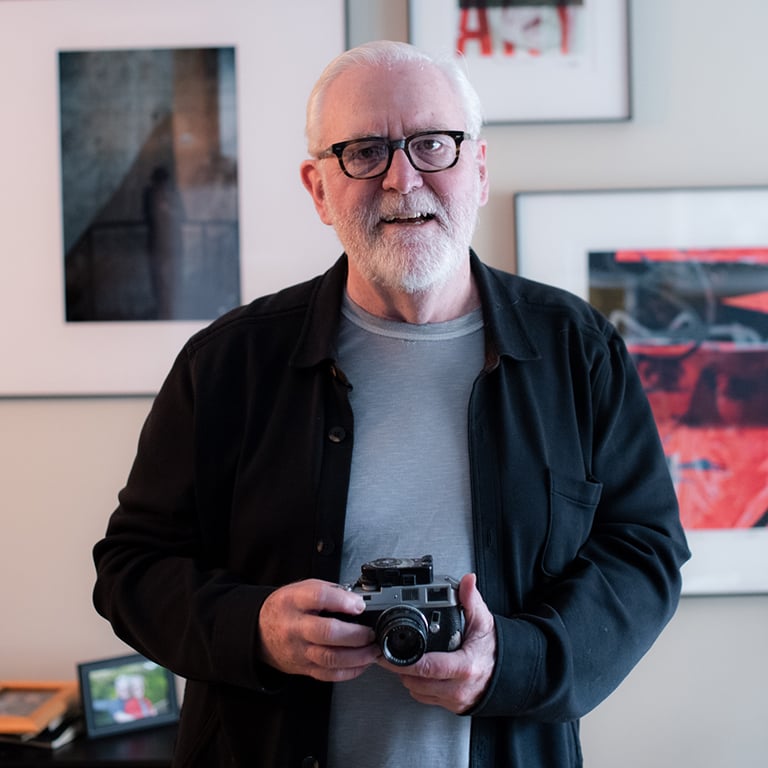 Max Steele holding camera in front of framed art